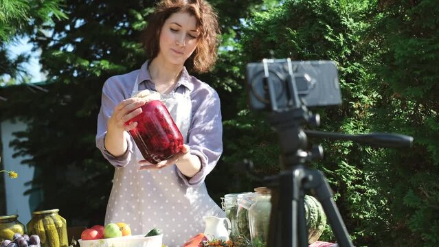 A woman shoots a video on a smartphone, compotes for the winter. On a warm autumn day, a housewife leads a video blog, teaches her subscribers how to preserve berries and fruits, and shows a jar with