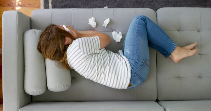 Frustrated woman covering face and crying, lying on sofa at home alone