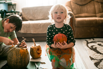 Fototapeta premium Smiling brother and sister create jack-o'-lanterns, bringing Halloween magic to life.