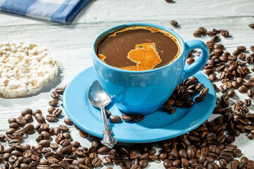 Blue cup of coffee with foam on a wooden table surrounded by scattered coffee beans