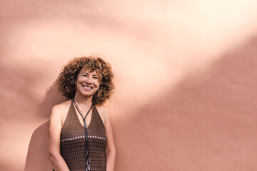 mature woman about 55 years old posing in front of a light brown wall