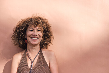 mature woman about 55 years old posing in front of a light brown wall