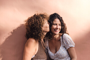 Mother and daughter posing smiling and in complicity in front of a brown wall.