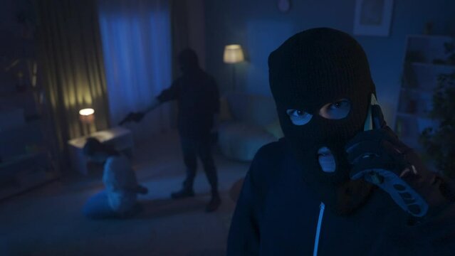 Video of two burglars holding a young woman hostage. One of them is pointing a gun at the victim, the other is talking on a phone and gives the terms of the ransom. HDR BT2020 HLG Material.