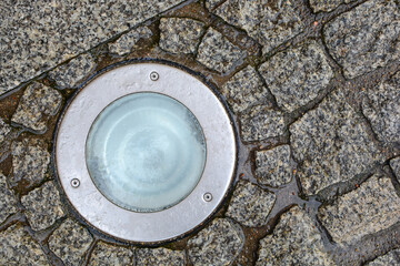 Close-up of a stone pavement with an illuminating round lamp, wet from the rain. Pavement...