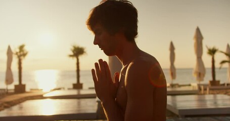 Close-up shot of a guy meditating on a sunny beach in the morning
