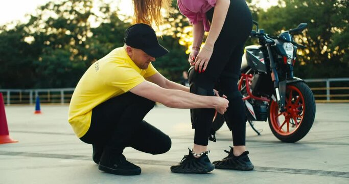 Instructor in a driving school in a yellow t-shirt helps a girl put on protective plates for riding a motorcycle. Knee pads and other protection for riding a motorcycle