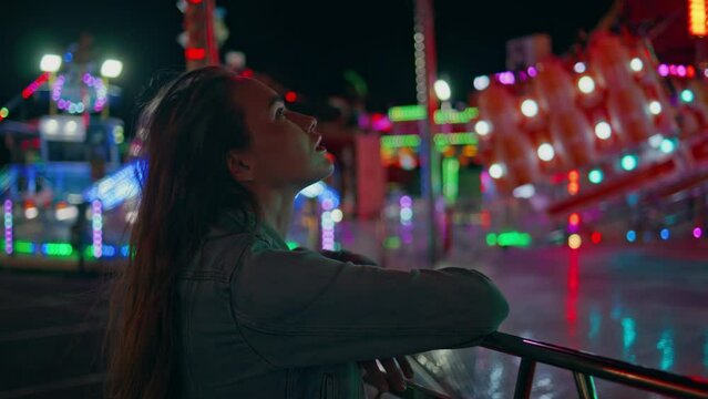 Amazed girl watching funfair carousel closeup. Dreamy young woman resting neon