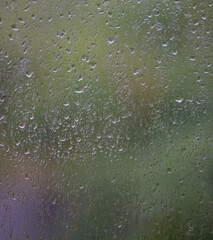 Water or rain droplets on glass or plastic on outdoor window with green background or backdrop signifying weather rain spring water wet or use for graphic backdrop  background or wallpaper