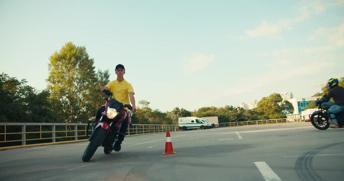 Overview of the guy instructor in a driving school in a yellow T-shirt. The motorcycle driver skillfully bypasses the obstacles in the form of orange cones