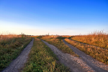 Dirt road in a field at sunset, rural landscape with blue sky