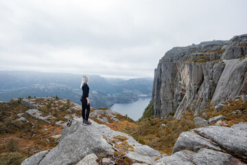 Obraz premium a girl standing on the edge of the cliff in the mountains on a hike in Norway on fjord