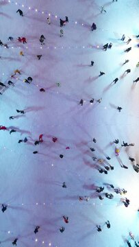 People ride on an ice rink on a winter evening during Christmas and New Year. Aerial view. Aerial vertical, vertical video background.