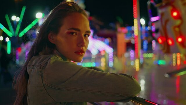 Neon woman enjoying evening at funfair closeup. Beautiful girl watching carousel