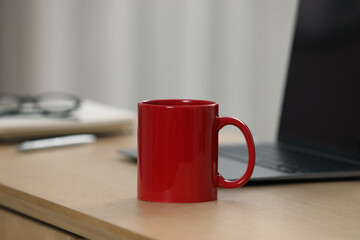 Red ceramic mug and laptop on wooden table at workplace