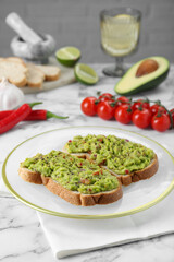 Delicious sandwiches with guacamole and ingredients on white table