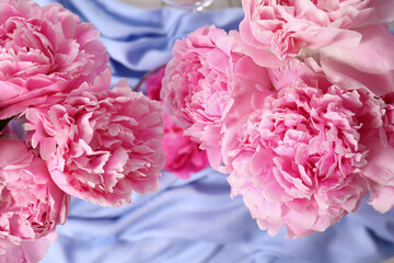 Beautiful aromatic peonies on light blue fabric, flat lay