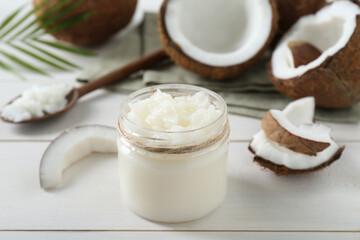 Jar of organic coconut cooking oil and fresh fruits on white wooden table, closeup