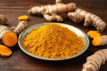 Plate with aromatic turmeric powder and cut roots on wooden table, closeup