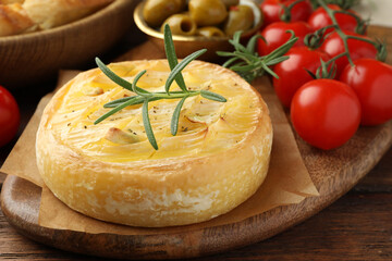 Tasty baked brie cheese with rosemary and cherry tomatoes on wooden table, closeup