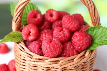 Tasty ripe raspberries and green leaves in wicker basket, closeup