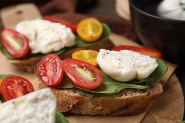 Delicious sandwiches with burrata cheese and tomatoes on board, closeup