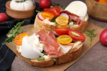 Delicious sandwiches with burrata cheese, ham, radish and tomatoes on brown textured table, closeup