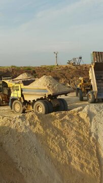 Haul Trucks conceal ground on open coal quarry. Dump Trucks. A heavy dump truck unloads sand. Sand pours from the truck. Aerial vertical,&nbsp;vertical video background.