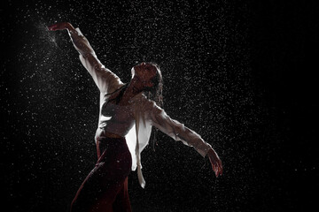 Dancing in the rain. A young woman in wet clothes dancing among water droplets, photo in the aqua studio. beautiful silhouette, model in a white shirt - 645542223