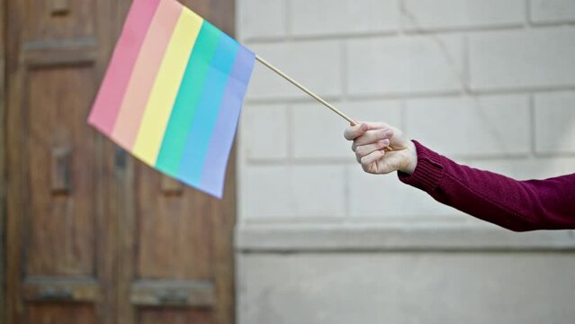 Young hispanic man holding rainbow flag at street