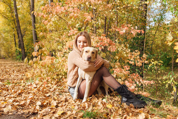 A young woman walking with her beloved labrador dog in autumn park.