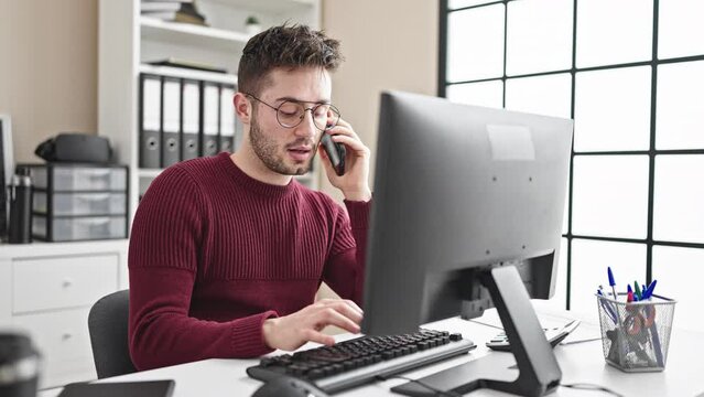 Young hispanic man business worker using computer talking on smartphone at office
