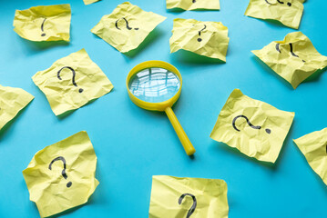 QnA or questions and answers concept. Yellow magnifying glass with question symbol on memo note over a blue background.