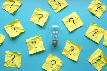 Light bulb with a questions symbol written on a yellow paper over a blue background.