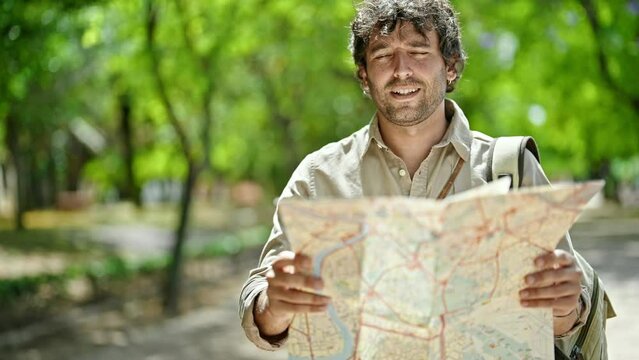 Young hispanic man tourist smiling confident looking at map at park