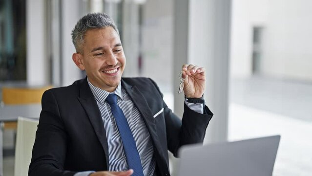 Young hispanic man real state agent having video call holding new house keys at office