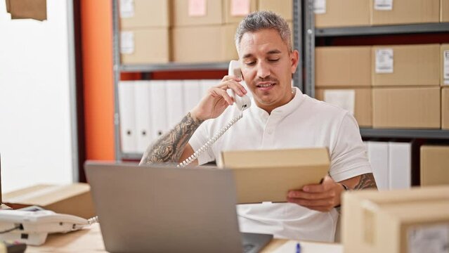 Young hispanic man ecommerce business worker talking on telephone holding package at office