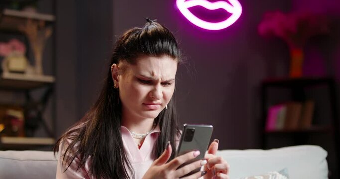 Woman scrolls through feed on social networks from smartphone. Woman frowns, looking at phone screen with disgruntled incredulous face. Feelings of jealousy, abhorrence, disgust. Unpleasant nasty news