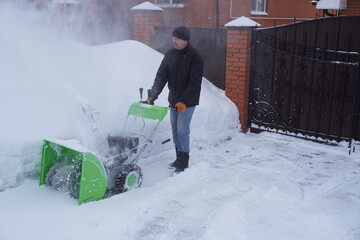 A man cleans snow in the winter in the courtyard of the house,  man cleaning snow with a snow blower