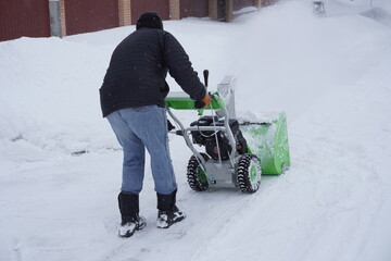 A man cleans snow in the winter in the courtyard of the house,  man cleaning snow with a snow blower