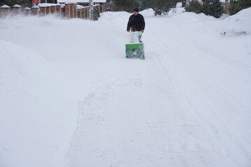 A man cleans snow in the winter in the courtyard of the house,  man cleaning snow with a snow blower