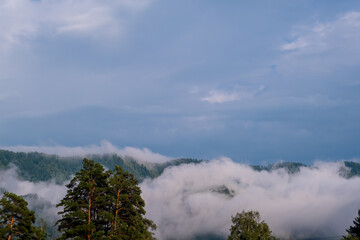 Mountains and peaks in fog at sunrise or sunset. Sun from behind the mountain. Amazing view of mountains and forest landscape with cloudy skies Altai mountains. Mountains and peaks in fog at sunrise