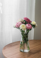 Bouquet of autumn aster flowers in a glass vase on a wooden round table