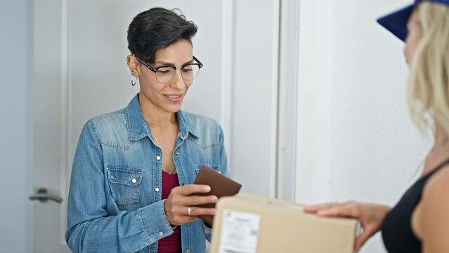 Young beautiful hispanic woman receiving package paying with dollars at home