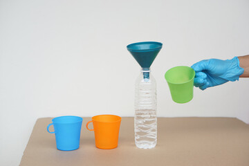 Closeup hand wear blue glove holds green mug to pour water into bottle to do science experiment....