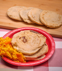 Savor the rich flavors of El Salvador with pupusas, a traditional Central American dish, served with curtido and savory sauce on a rustic wooden board