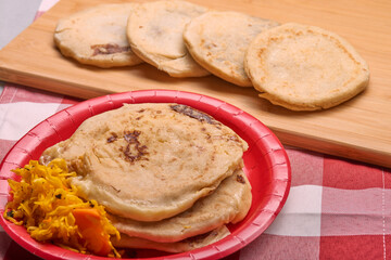 Savor the rich flavors of El Salvador with pupusas, a traditional Central American dish, served with curtido and savory sauce on a rustic wooden board