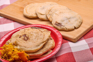Savor the rich flavors of El Salvador with pupusas, a traditional Central American dish, served with curtido and savory sauce on a rustic wooden board