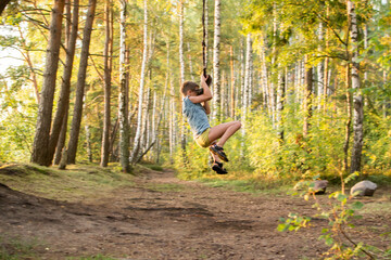 A young guy, a teenage boy, rides a bungee, on a rope in a forest among birches on the lake.
