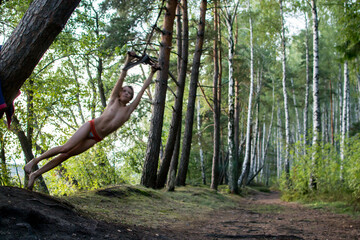 A young guy, a teenage boy, rides a bungee, on a rope in a forest among birches on the lake.